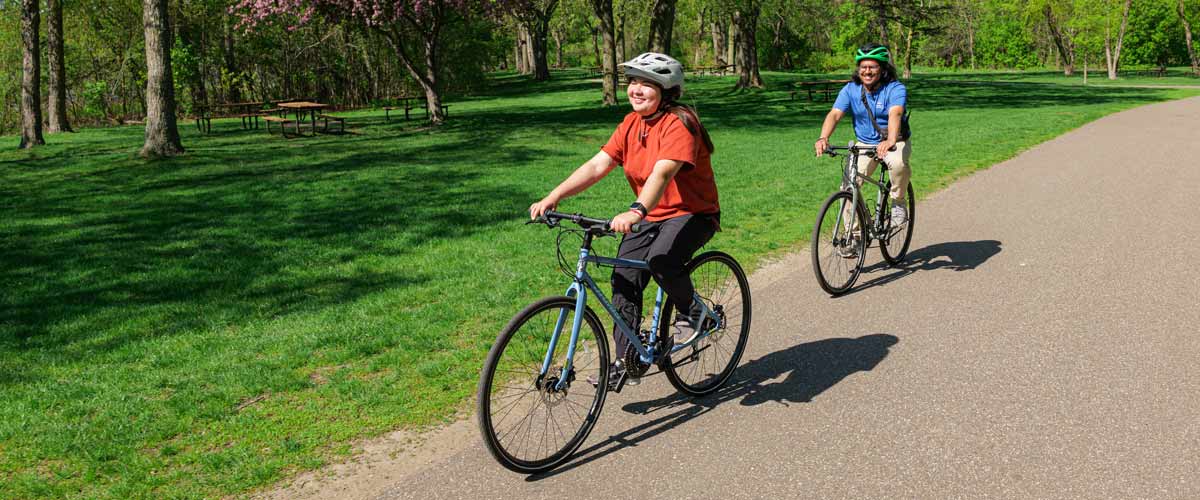 Three cyclists merging onto a shared riverside bike path at dawn